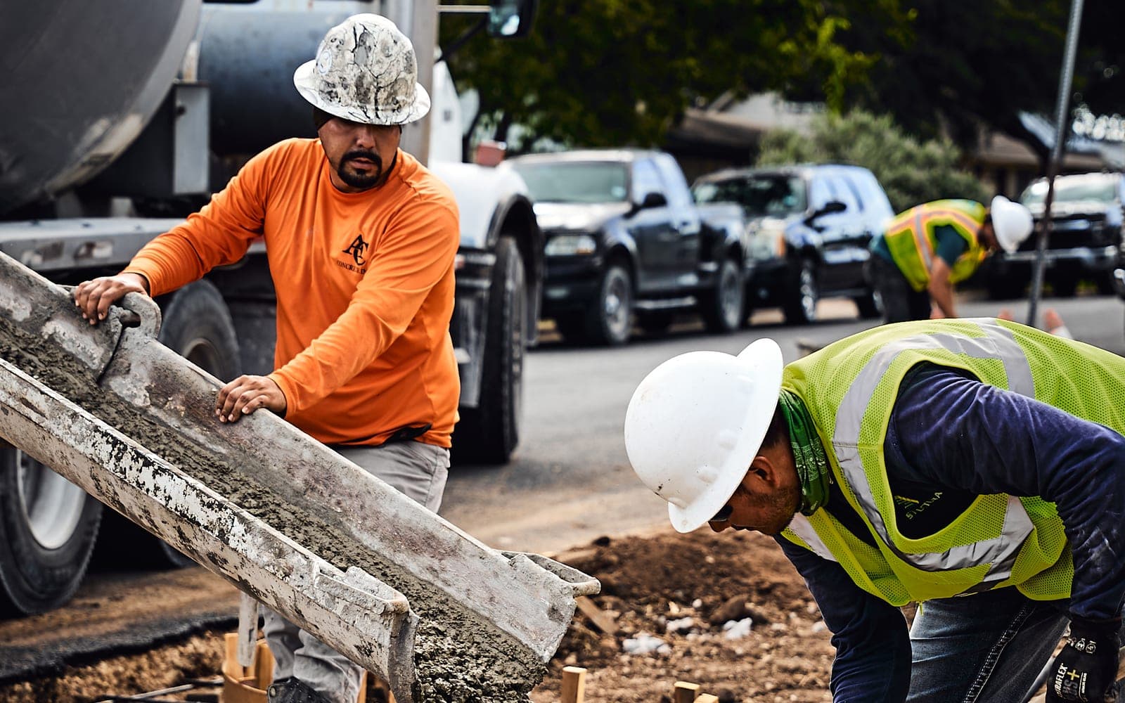 Workers in hard hats guiding concrete from a truck chute into foundation forms