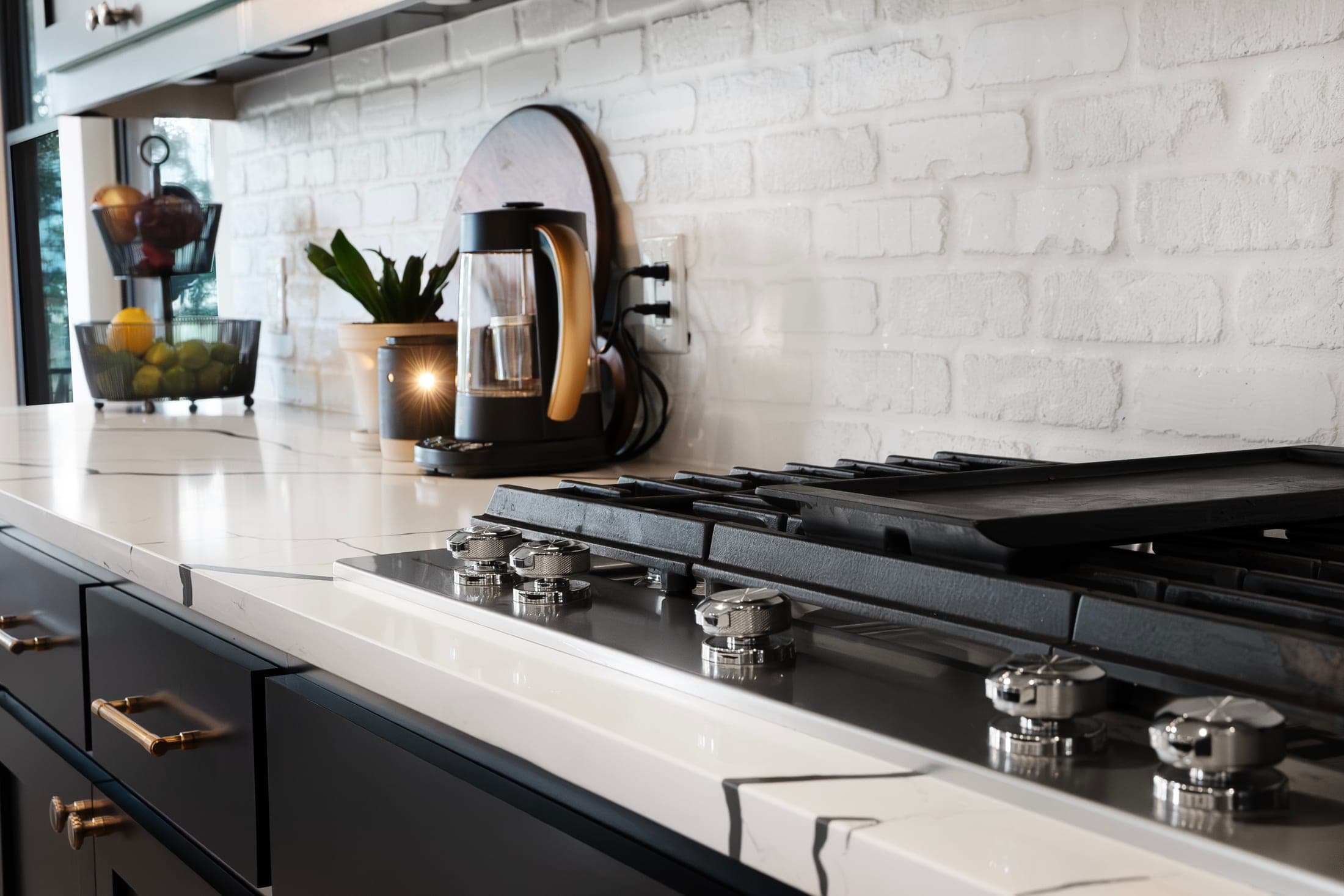 A gas cooktop set into a white countertop against a white brick backsplash, black cabinets below