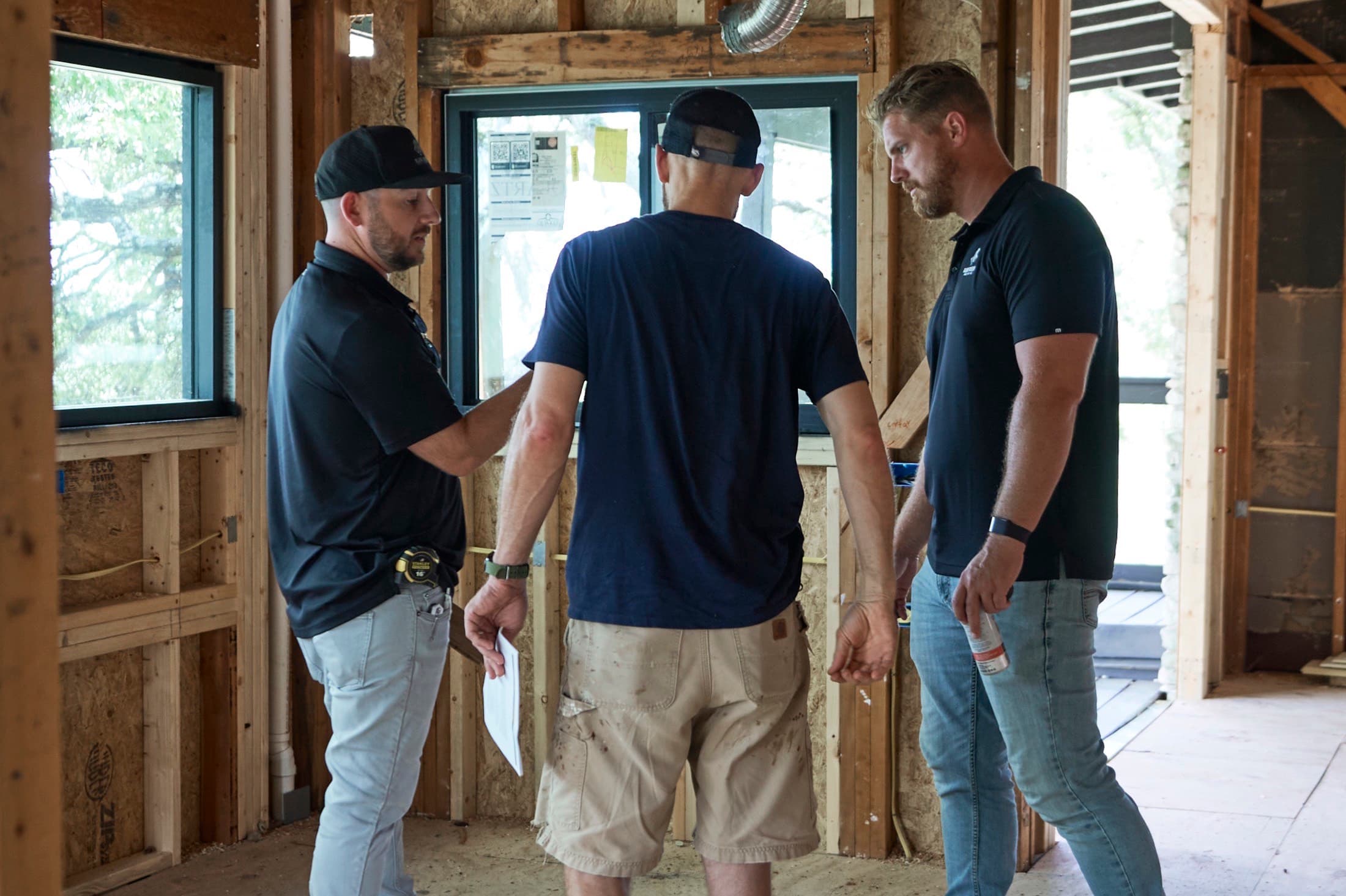 Three people reviewing the framing inside a house under construction, one holding plans