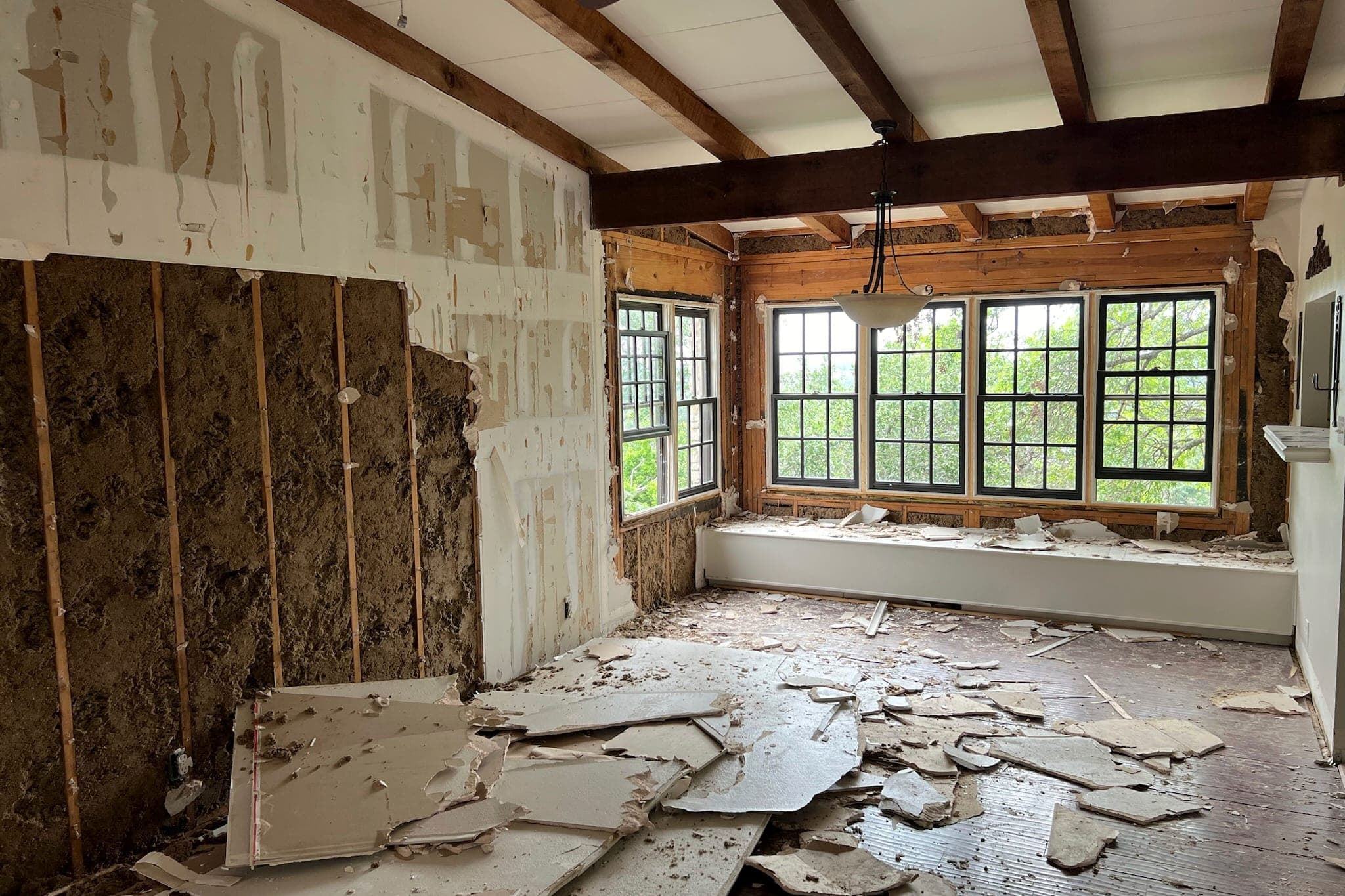 A room mid-demolition: drywall torn off to the insulation and debris across the floor