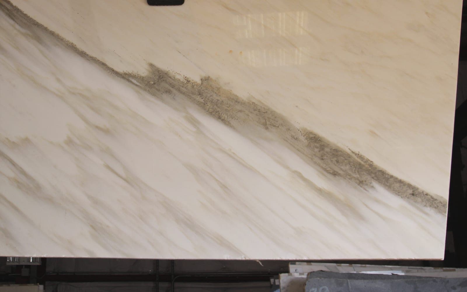 A polished Calacatta marble slab hanging from a vacuum lifter, a dark vein cutting diagonally across it