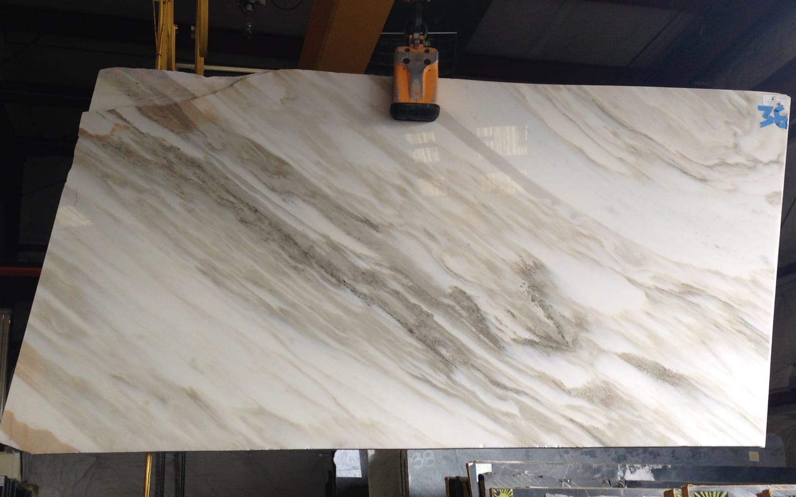 A full slab of polished Calacatta Bella marble on a vacuum lifter in a stone yard warehouse