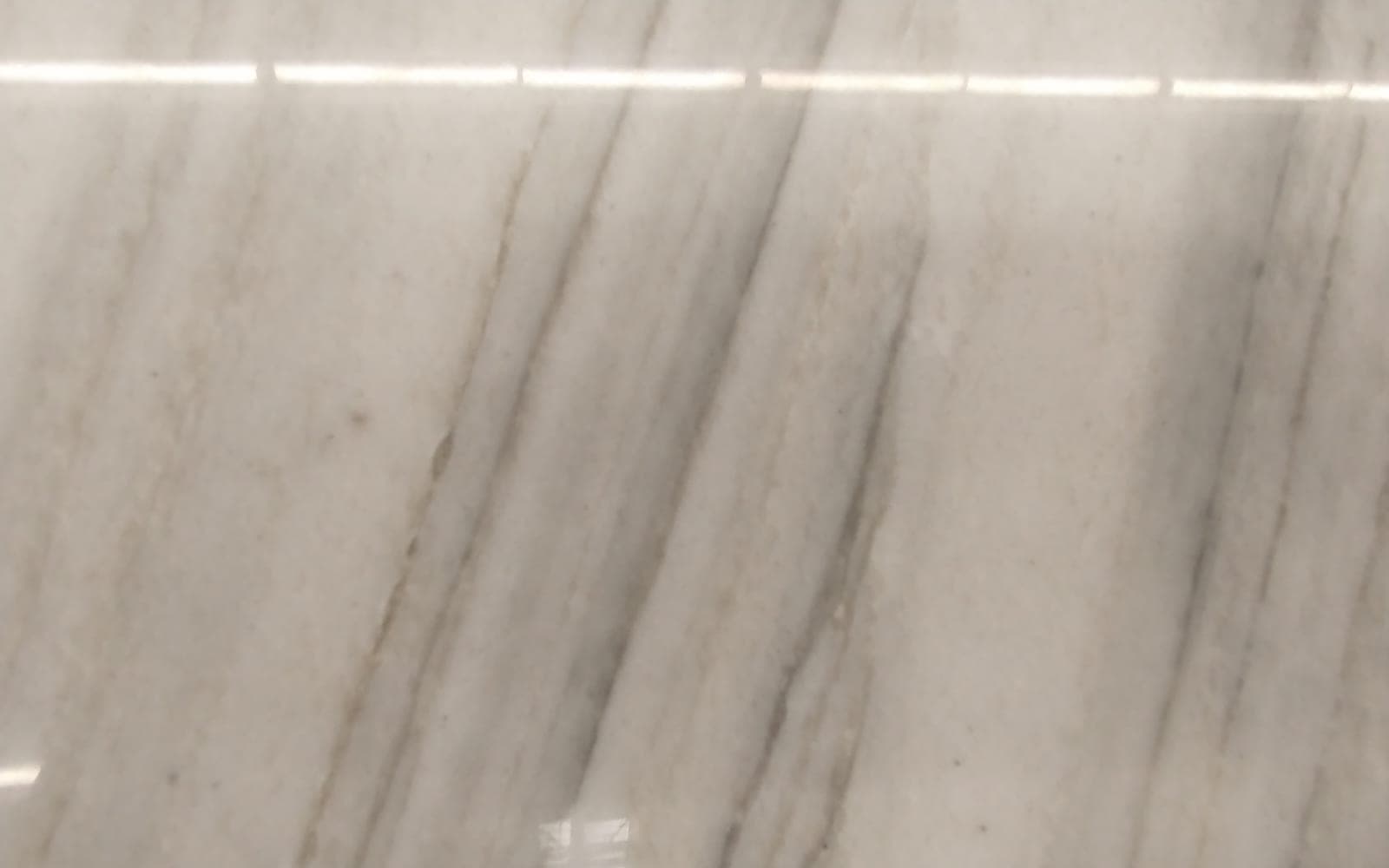 A polished quartzite slab with diagonal grey veining, showroom lights reflected along its top edge