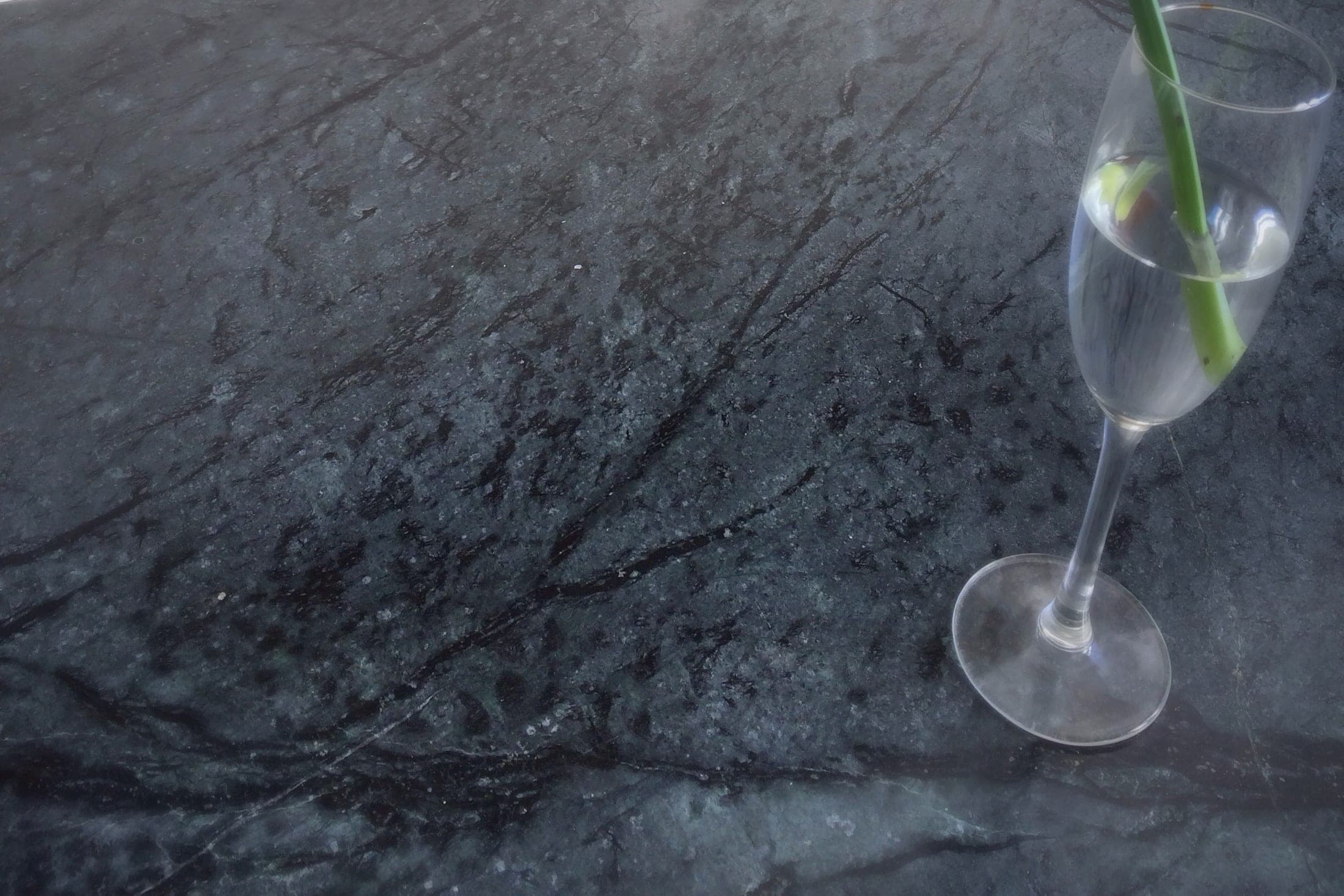 A charcoal soapstone kitchen counter with dark veining, a glass holding a flower stem resting on it