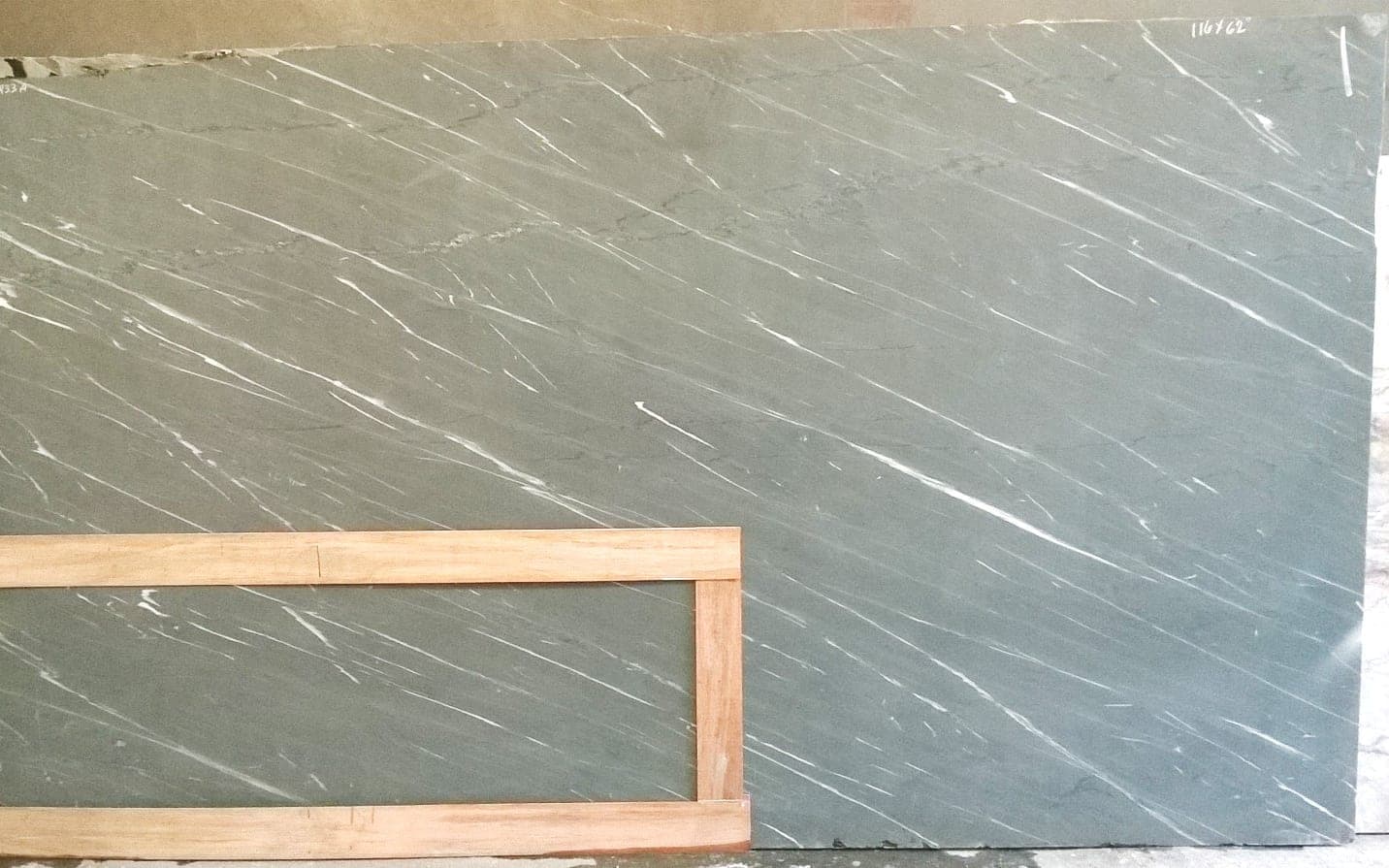 A grey soapstone slab with white veining at a stone supplier, a wooden countertop template laid over its lower left